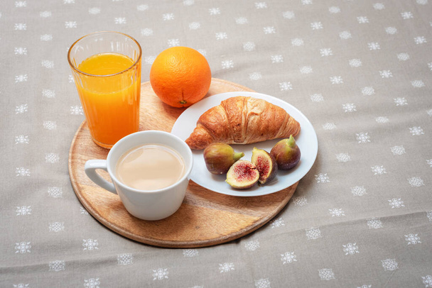 Croissant en un plato con higos, una taza de café, jugo de naranja y una naranja en una bandeja. Concepto de desayuno tradicional - Foto, imagen