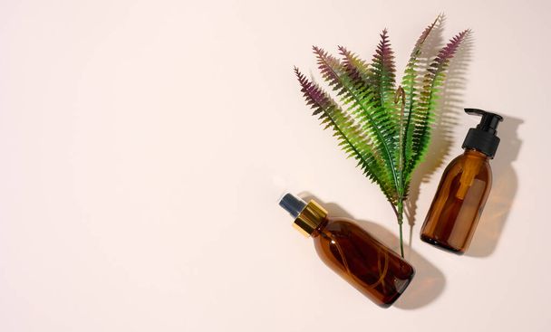 brown glass bottles with dispenser and a sprig of fern on a beige background. Packaging for gel, serum, advertising and promotion. Natural organic products. Mock up - Photo, Image