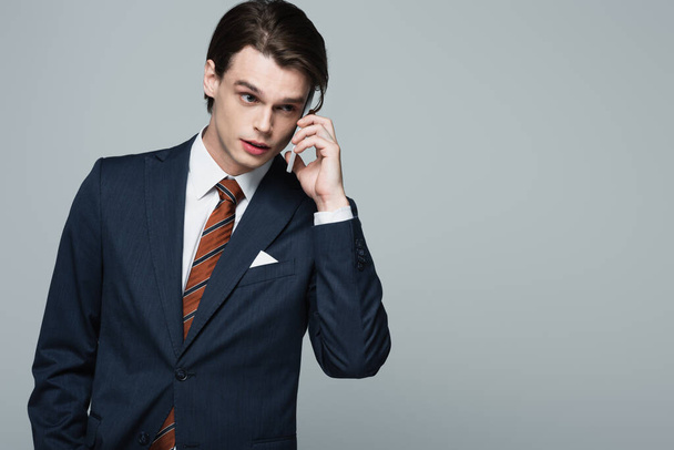 young businessman in suit talking on smartphone isolated on grey - Fotó, kép