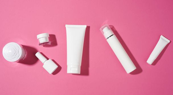 ネイルポリッシュ、ジャーとピンクの背景に化粧品のための空の白いプラスチックチューブ。クリーム、ゲル、血清、広告および製品プロモーションのためのパッケージ、トップビュー - 写真・画像