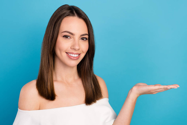 Photo of cute brunette young lady hold empty space wear white top isolated on blue color background - Φωτογραφία, εικόνα
