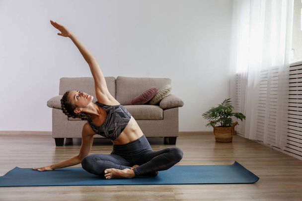 Sporty young woman practicing yoga in the comfort of her own home. Yogini performing morning physical exercise routine at the living room. Interior background, copy space, close up. - Foto, immagini