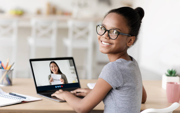 Uśmiechnięta młoda, mądra studentka w okularach studiująca w domu online z tysiącletnim korepetytorem azjatyckim na ekranie gadżetu - Zdjęcie, obraz