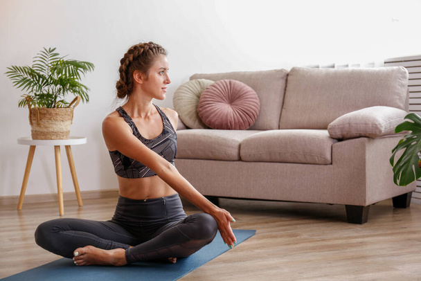 Sporty young woman practicing yoga in the comfort of her own home. Yogini performing morning physical exercise routine at the living room. Interior background, copy space, close up. - Foto, Bild