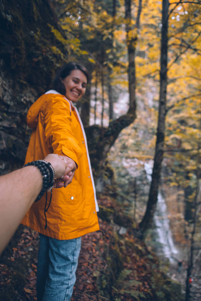 sígueme concepto mujer en impermeable amarillo caminando por el sendero a la estación de otoño de cascada del bosque - Foto, imagen