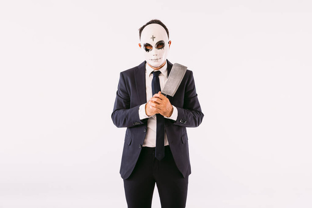Öltönyt és nyakkendőt visel, gyilkos maszkot kereszttel a homlokán Halloweenkor, késsel fenyegetve. Karnevál és halloween ünneplés - Fotó, kép