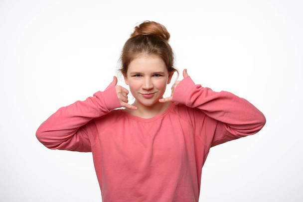 Πάρε με αργότερα. Η σκεπτική νεαρή κοπέλα κάνει τηλεφωνική χειρονομία, προσποιείται την κινητή επικοινωνία, φοράει ροζ φούτερ. Έννοια γλώσσας σώματος. Στιγμιότυπο στούντιο, λευκό φόντο - Φωτογραφία, εικόνα