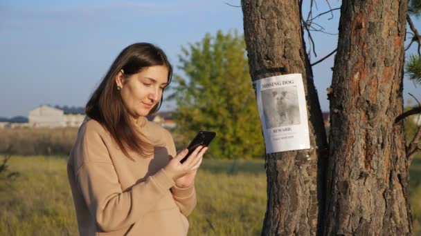 Mujer con capucha marca el número del cartel del perro desaparecido en el parque - Metraje, vídeo
