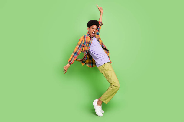 Photo of charming sweet dark skin man wear plaid shirt smiling dancing showing v-signs isolated green color background - Fotó, kép