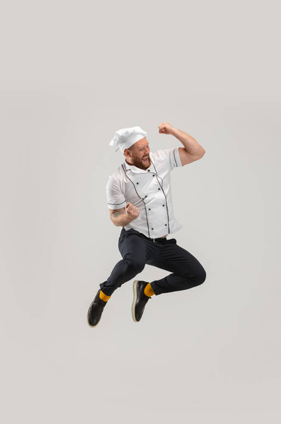 One Caucasian bearded man, chef in uniform jumping high isolated on white background. Concept of job, occupation, humor. - Fotó, kép