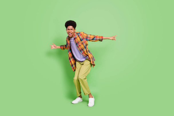 Photo of funky sweet dark skin man wear plaid shirt smiling dancing isolated green color background - Zdjęcie, obraz