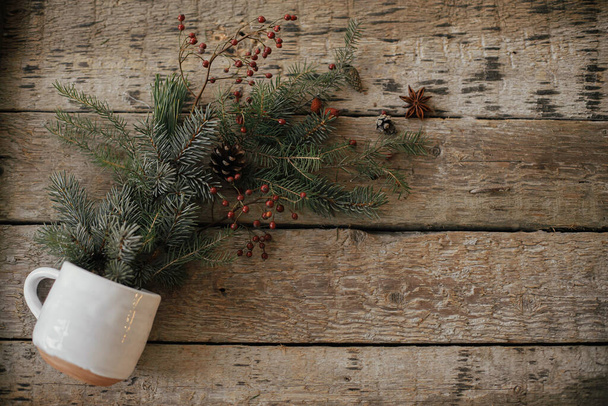 こんにちは冬。スプルースの枝、赤い果実、松のコーンをこぼしたスタイリッシュなカップと素朴な古い木製の背景フラットレイアウト上のアニス。休日の準備。メリークリスマス！テキストのスペース - 写真・画像