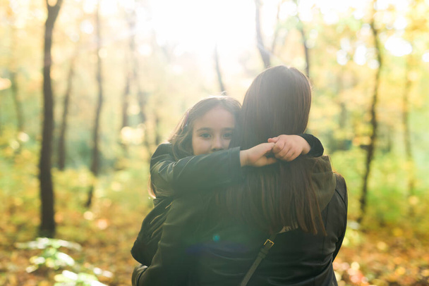 Mother and daughter spend time together in autumn yellow park. Season and single parent concept. - 写真・画像