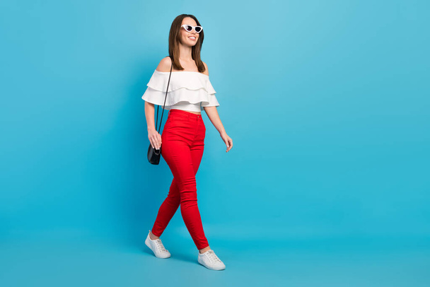 Full length photo of charming young positive happy woman walk look empty space sunglass isolated on blue color background - Photo, image