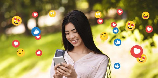 幸せな若いアジアの女性学生がソーシャルネットワークでチャット,ブログ,公園でメッセージを入力 - 写真・画像