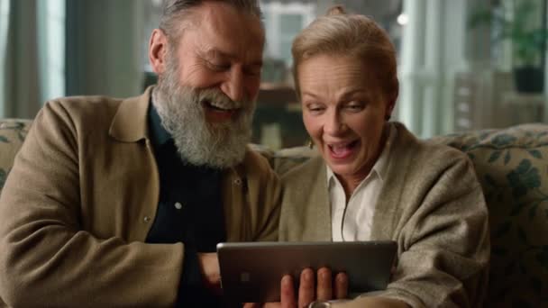 Смеющаяся зрелая пара смотрит планшетный экран на диване в классической гостиной. - Кадры, видео
