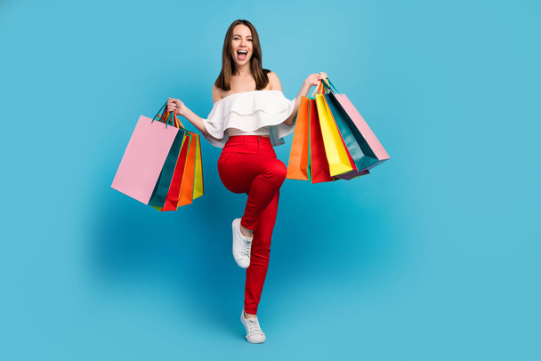 Full body photo of pretty amazed cheerful woman hold hands shopping bag winner isolated on blue color background - Fotoğraf, Görsel