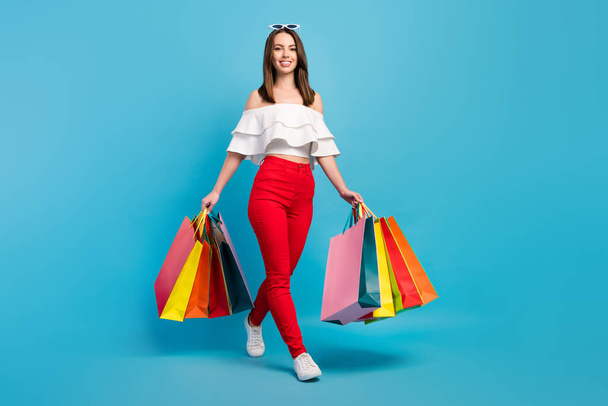 Full length photo of happy pretty charming woman walk hold hands shopping bags isolated on blue color background - Fotografie, Obrázek