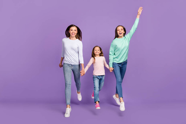 Photo of sweet funny daughters mom dressed casual sweaters holding hands jumping high isolated purple color background - Photo, image