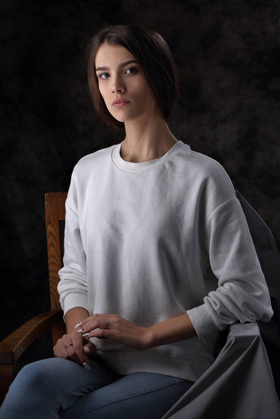 Studio portrait of a beautiful girl sitting in a chair on a dark background - Fotó, kép