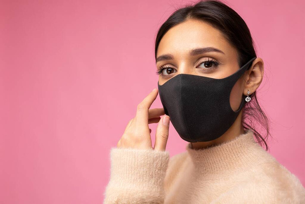 Felnőtt bájos nő újrahasznosítható vírus védő fekete maszk az arcon ellen coronavirus izolált a rózsaszín háttér fal - Fotó, kép