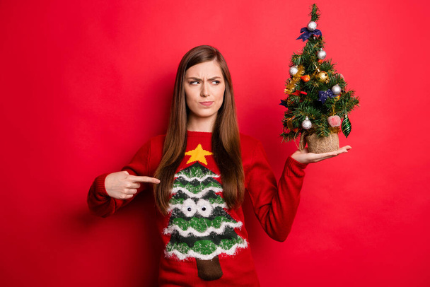 Photo of sad millennial lady point holiday sweater hold look little tree isolated on red color background - Foto, Imagem