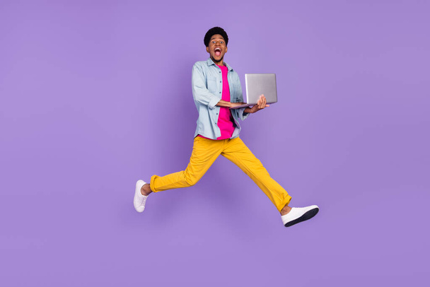 Photo of programmer guy jump hold netbook hurry late wear blue shirt pants shoes isolated purple color background - Foto, Imagem