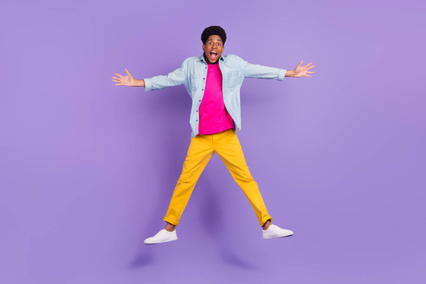 Photo of funky cheerful glad guy jump shout enjoy flight wear blue shirt isolated purple color background - 写真・画像