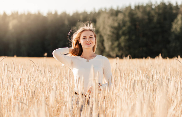 Uma jovem menina bonita em uma saia jeans caminha através de um campo de trigo em um dia ensolarado - Foto, Imagem