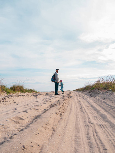 Šťastný otec a dcera běží skákání baví na prázdné podzimní pláži. Táta a dítě kráčející po bílé pískové cestě s rákosím modrého nebe pozadí. Životní styl skutečných lidí. Koncept šťastného cestování - Fotografie, Obrázek