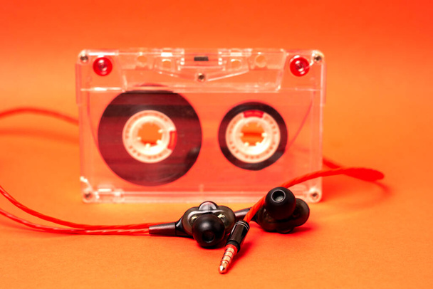 Audio cassette and in-ear headphones on an orange background. Selective focus. - Photo, Image