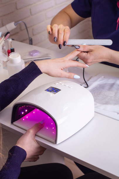 Female hand with manicure nails in gel polish lamp in beauty salon - Foto, immagini