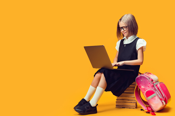 Full length smiling schoolgirl sit on the stack of books work on laptop. Kids education concept. - Foto, afbeelding