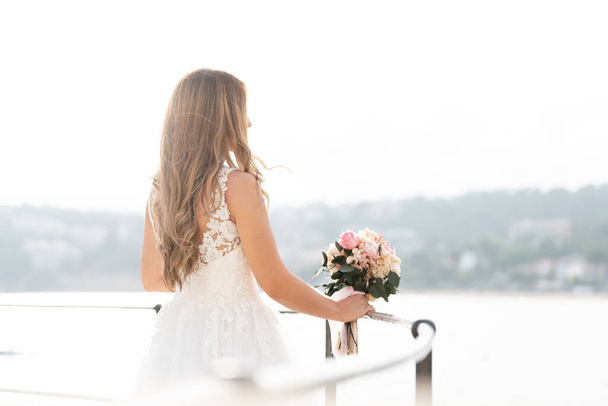 Brunette bride in white dress looking at the sea  - Φωτογραφία, εικόνα