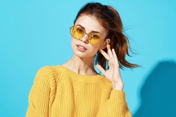 woman in yellow sweater holding her hair studio posing blue background - Photo, Image