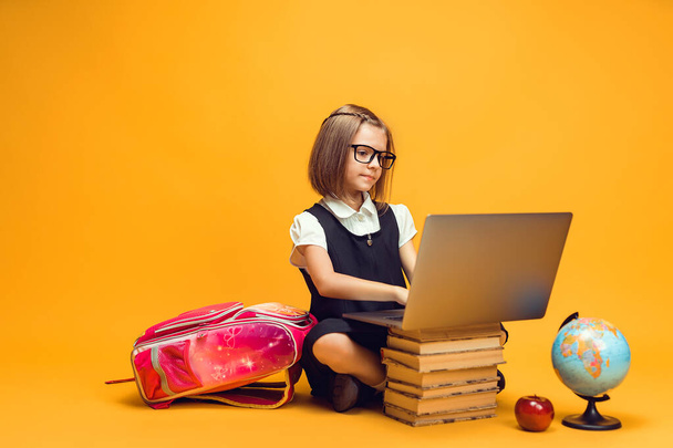 Full length caucasian schoolgirl sitting behind a stack of books working on laptop. Kids education  - Photo, image
