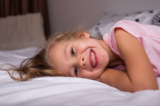 una niña feliz en pijama está acostada en la cama en el dormitorio - Foto, Imagen