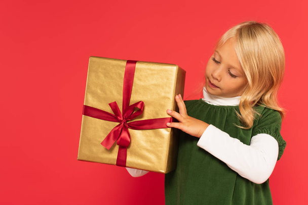 girl in green dress looking at present in golden wrapping paper on red - Foto, Bild