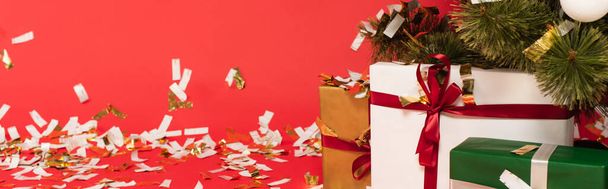 boîtes cadeaux multicolores près de l'arbre de Noël et confettis sur fond rouge, bannière - Photo, image
