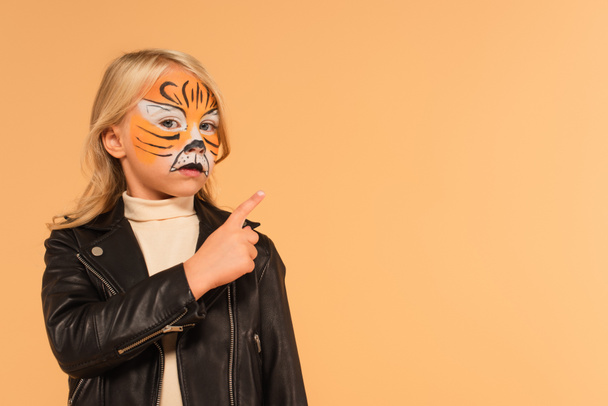 girl in leather jacket and tiger makeup pointing with finger isolated on beige - Fotó, kép