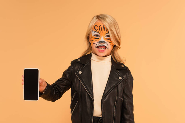 criança com pintura de rosto de tigre mostrando smartphone com tela em branco e rosnando isolado no bege - Foto, Imagem