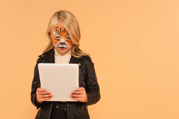 menina com pintura de rosto de tigre usando tablet digital isolado no bege - Foto, Imagem