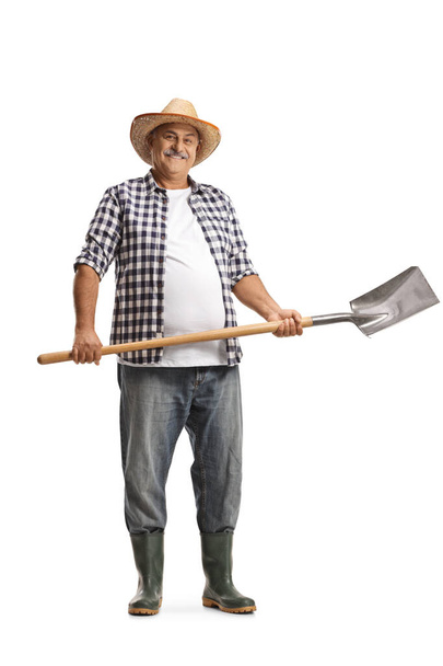 Full length portrait of a happy mature farmer with a spade isolated on white background - 写真・画像