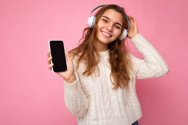 Szekrény portré fotó gyönyörű boldog mosolygós fiatal nő visel elegáns alkalmi ruhát elszigetelt háttér fali gazdaság és mutatja a mobiltelefon üres kijelző a mockup visel fehér - Fotó, kép