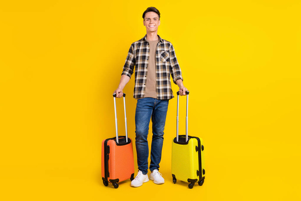 Photo of guy hold two bags beaming smile wear checkered shirt jeans footwear isolated yellow color background - Fotoğraf, Görsel