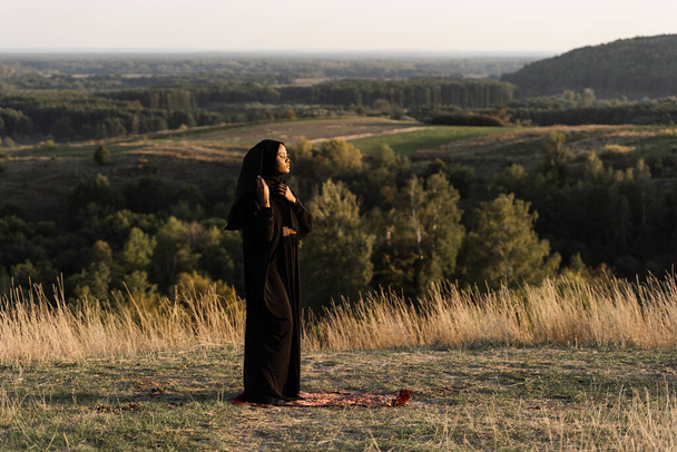 Czarna muzułmanka modląca się na dywanie. Solat modli się na pięknym wzgórzu. Salah tradycyjna modlitwa - Zdjęcie, obraz