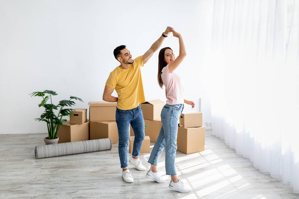 Affectionate multiraciale paar dansen in hun huis tussen kartonnen dozen op bewegende dag, vrije ruimte - Foto, afbeelding