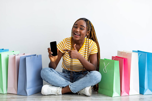 Emotionaalinen musta nainen shopaholic osoittaa matkapuhelin tyhjä näyttö - Valokuva, kuva