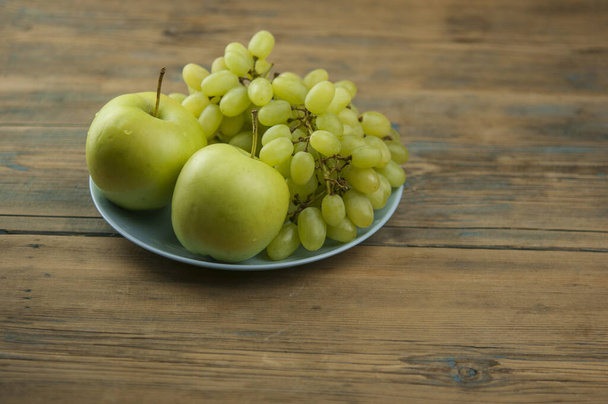 Teller mit köstlichen frischen Früchten wie Äpfeln und Trauben auf einem Tisch - Foto, Bild