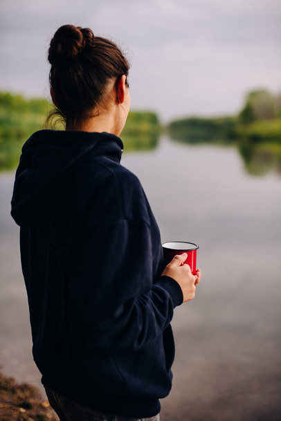 a girl holds a red mug on the shore of the lake - Foto, Imagen